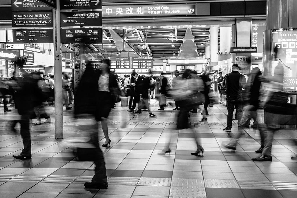 A black and white image of people walking quickly through a train station.