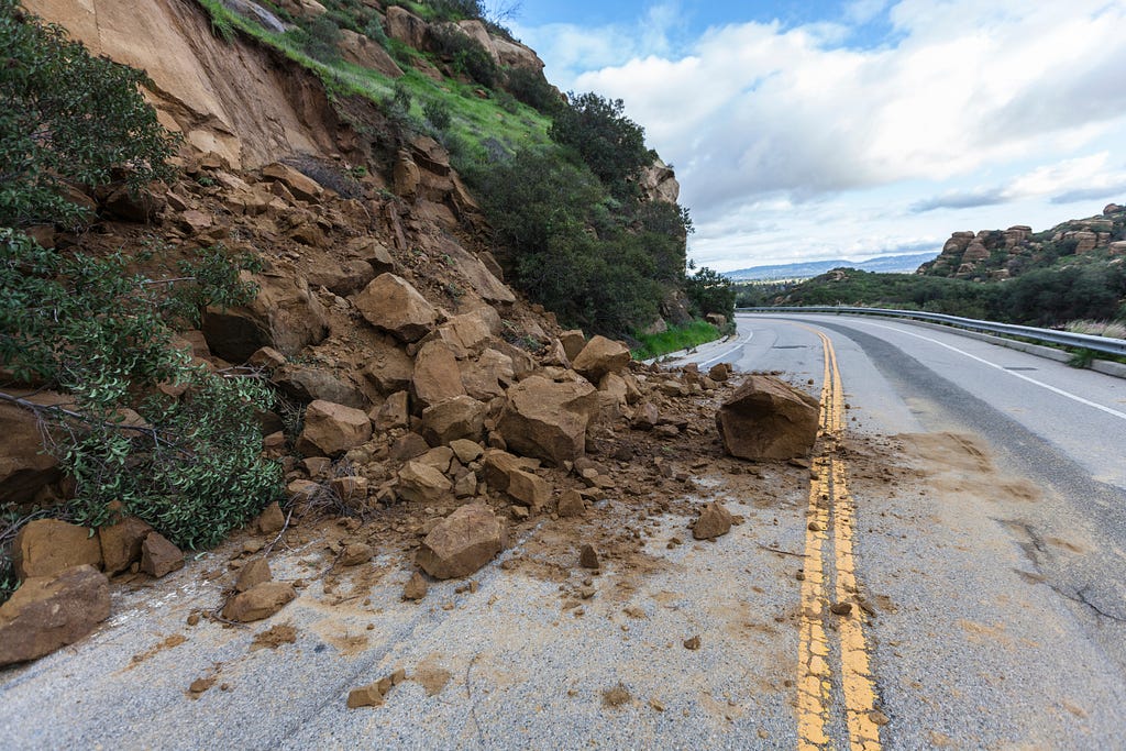 Image shows broken boulders from a hill alongside a road