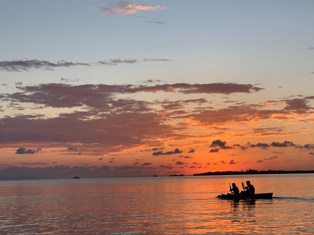 The silhouette of two people canoeing in the ocean against the backdrop of a beautiful, orange sunset in Utila.