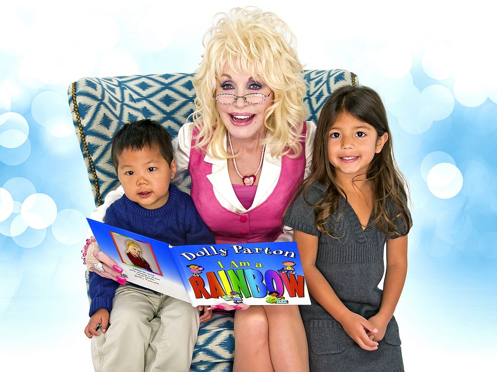 Dolly Parton poses with two children, holding a book open.