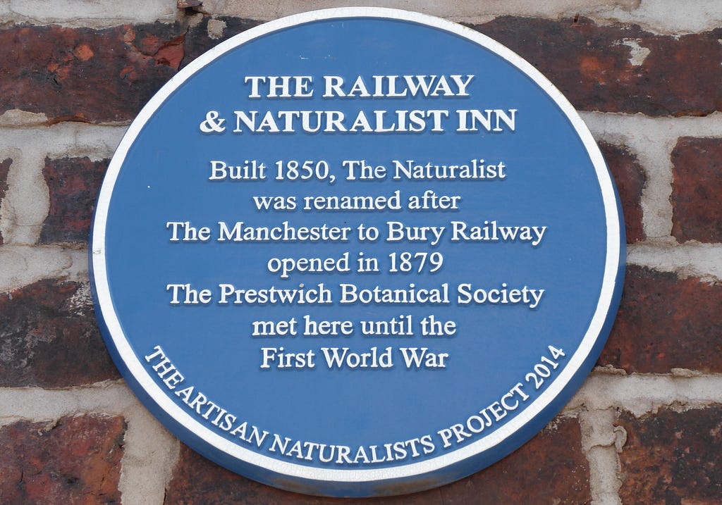 Round, blue plaque on the wall of the Railway & Naturalist Inn giving details of the pub’s history in white lettering.