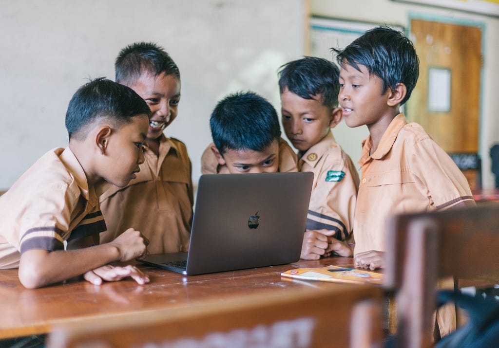 5 orang anak SD yang sedang melihat layar laptop macbook di kelas. foto ini mengilustrasikan pentingnya learn, unlearn, dan relearn dalam proses belajar