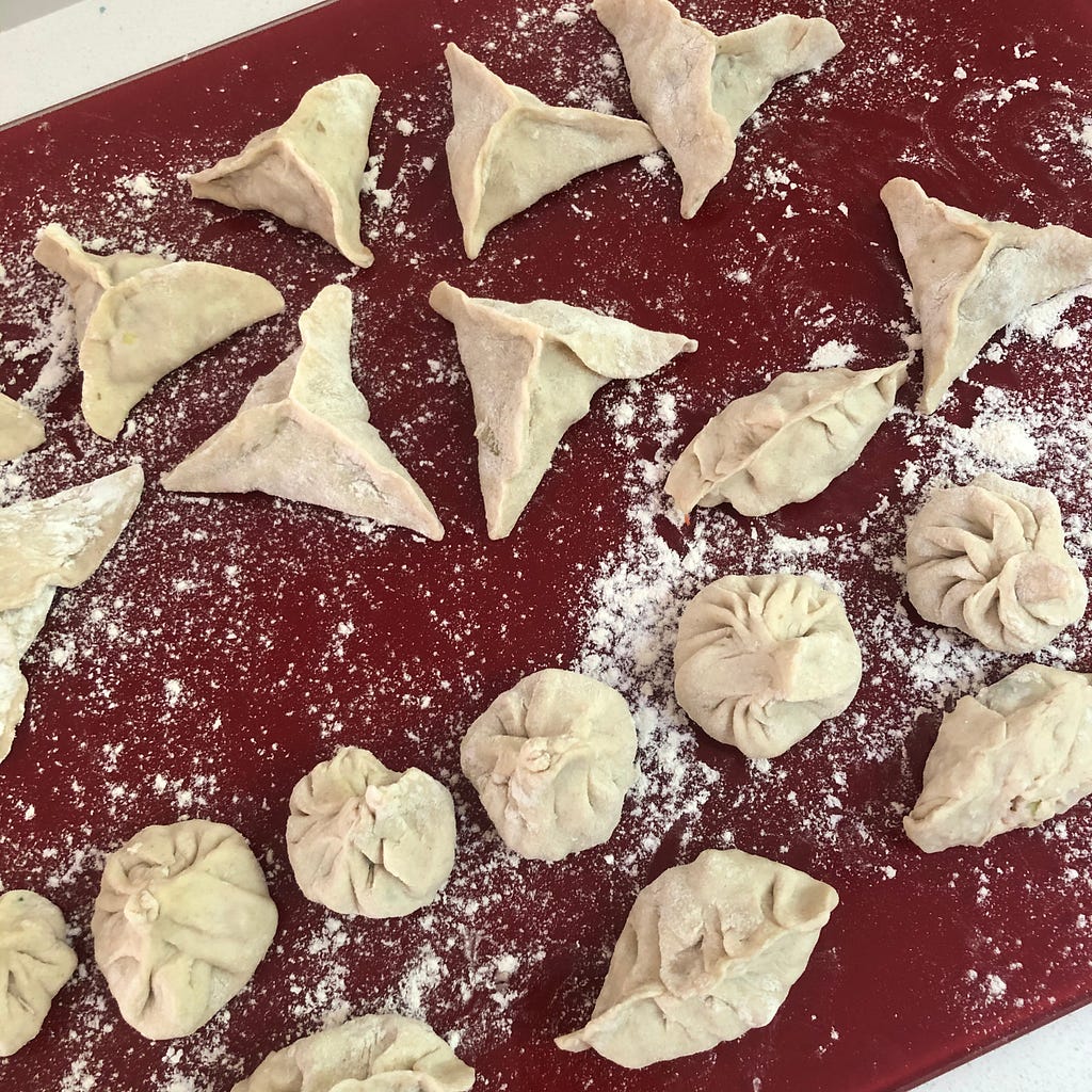 A tray of experimentally-folded Chinese-style dumplings made with my son. A range of shapes and sizes, ready to be steamed