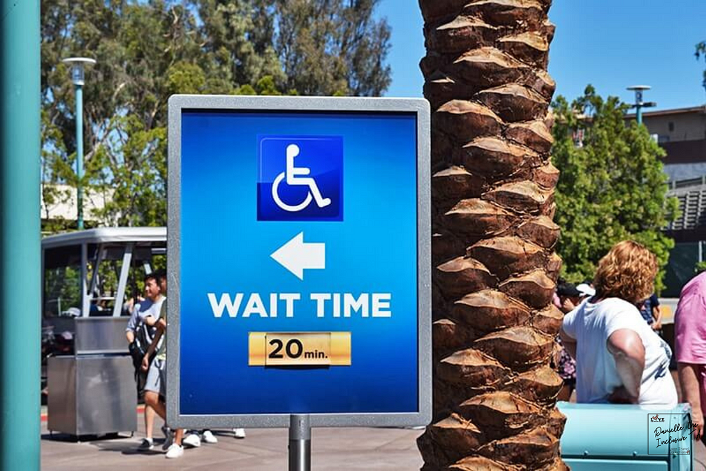 image depicts a blue sign with a picture of a wheelchair on it, with a directional arrow indicating the wait time for people in wheelchairs for this particular attraction