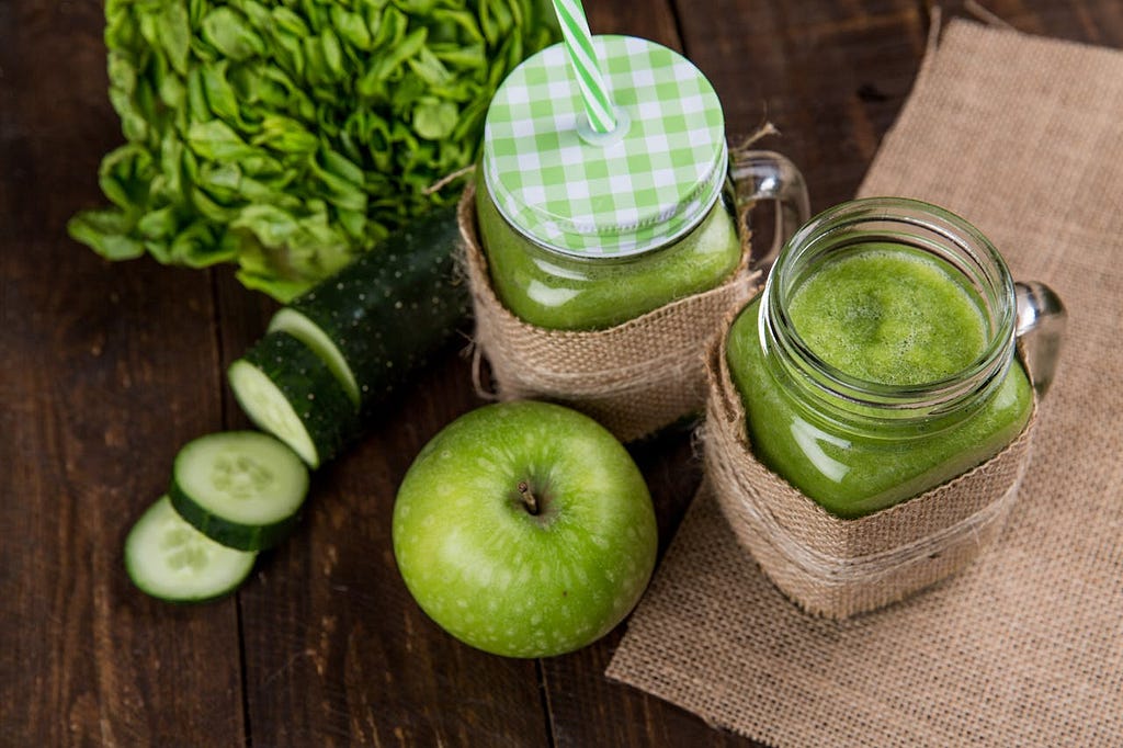 Two glass jars containing drinks, with a green apple beside them