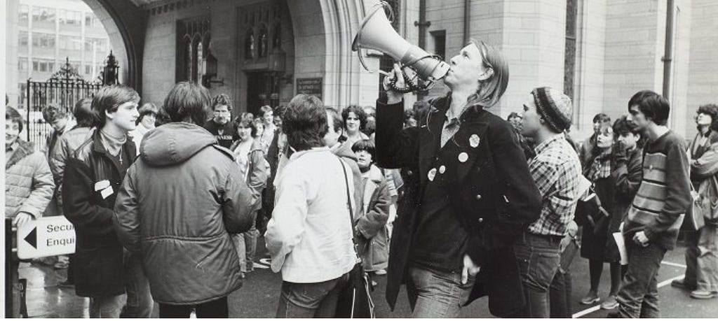 Group of students at a rally, central figure has a megaphone