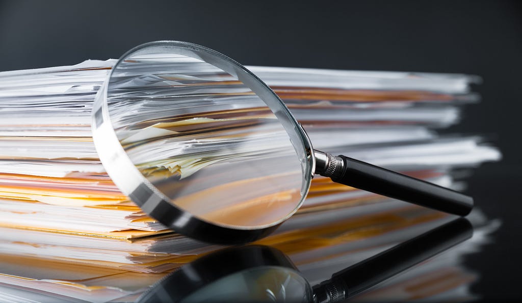 A magnifying glass leaning against a stack of reports. Photo by Sezeryadigar/Getty Images