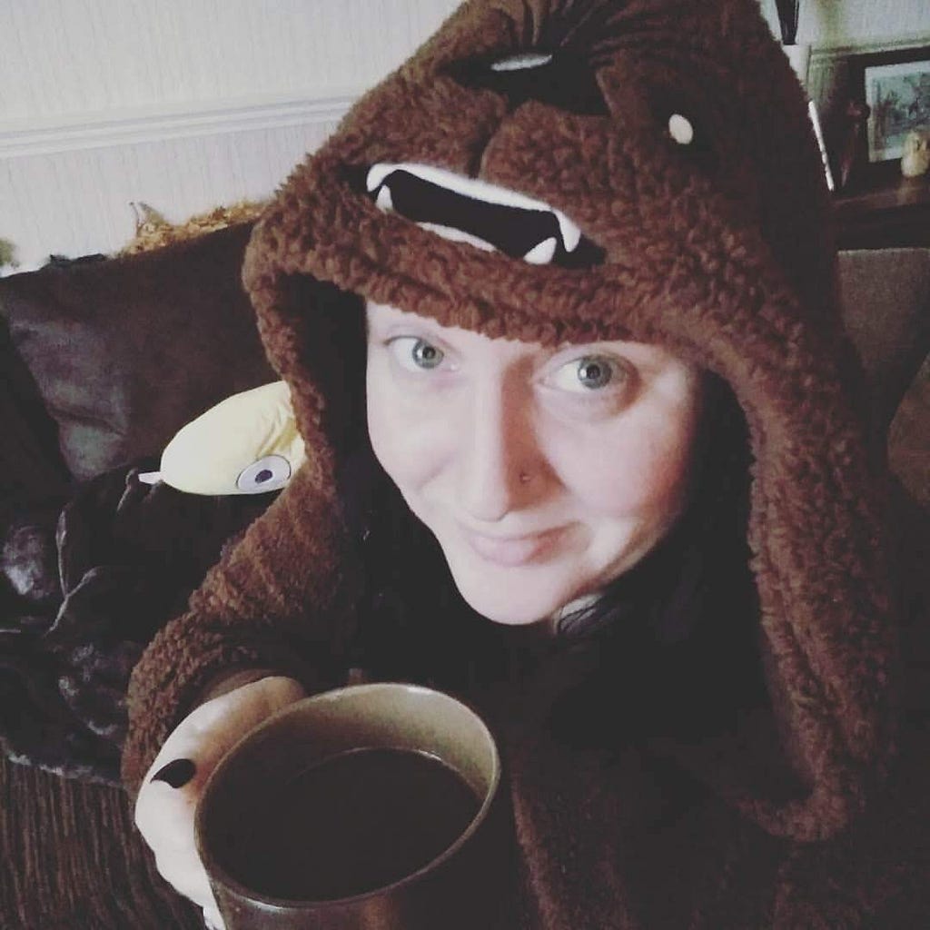 Selfie, a woman with long dark hair and blue eyes, sitting on the couch in her Chewbacca hoodie smiling and holding a hot drink in a mug.