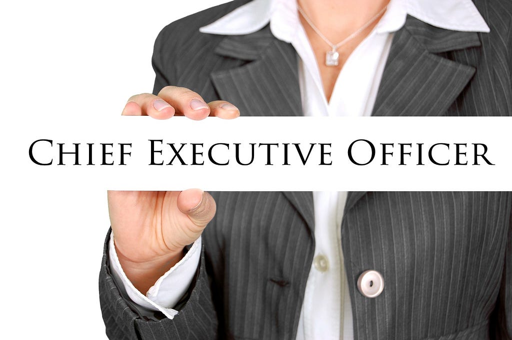 A woman wearing a suit holding a sign that says “Chief Executive Officer.”