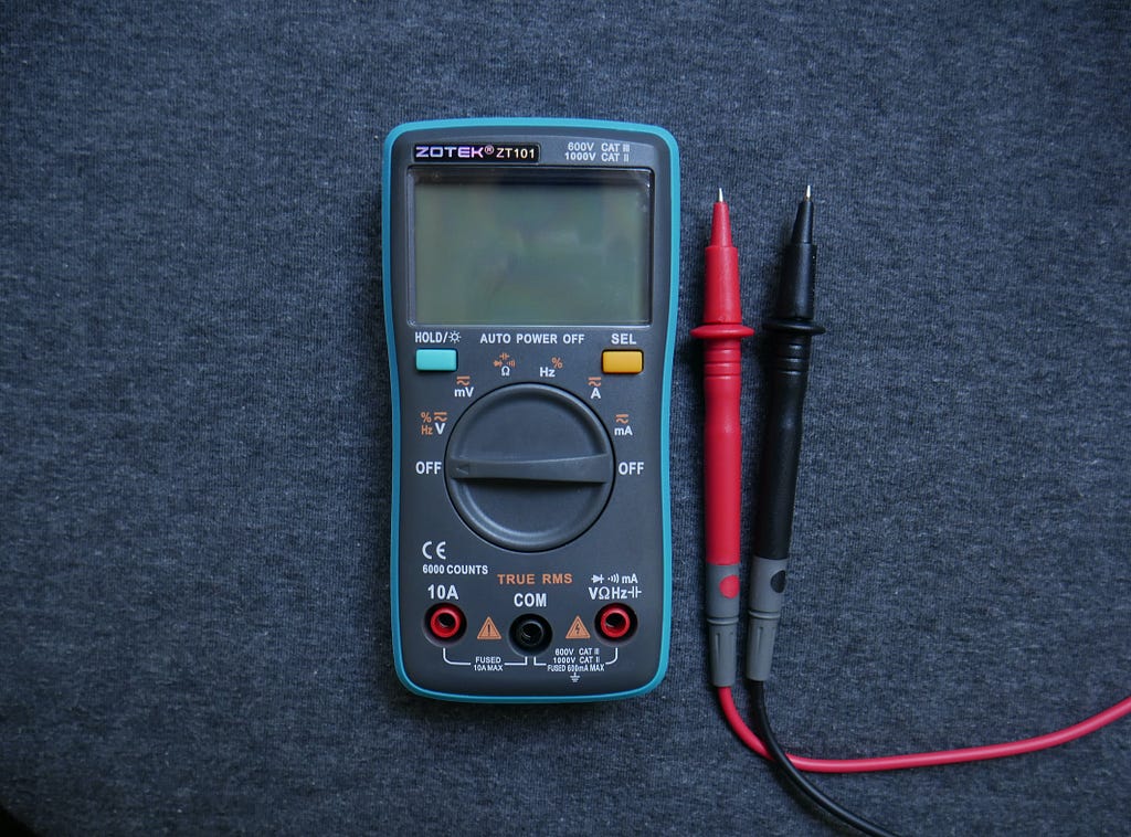 Blue multimeter with red and black prongs on a blue carpeted background