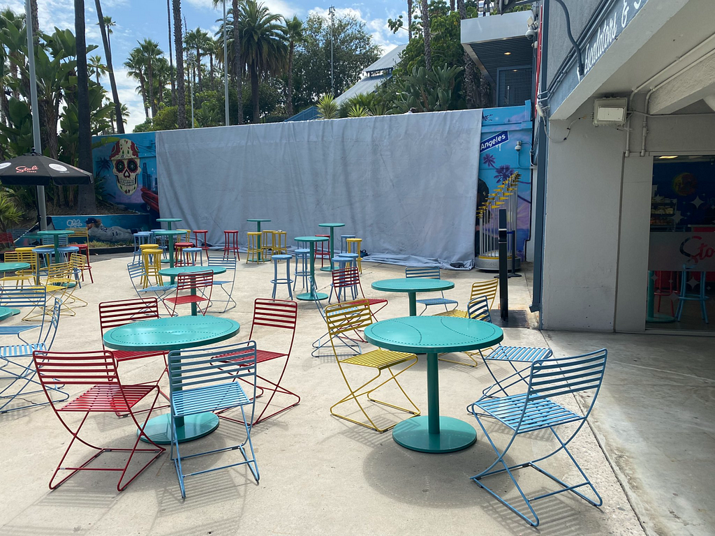 Picture of Dodger Stadium where the mural with Julio Urias has been covered with a white tarp. Colorful chairs and tables are in the foreground.