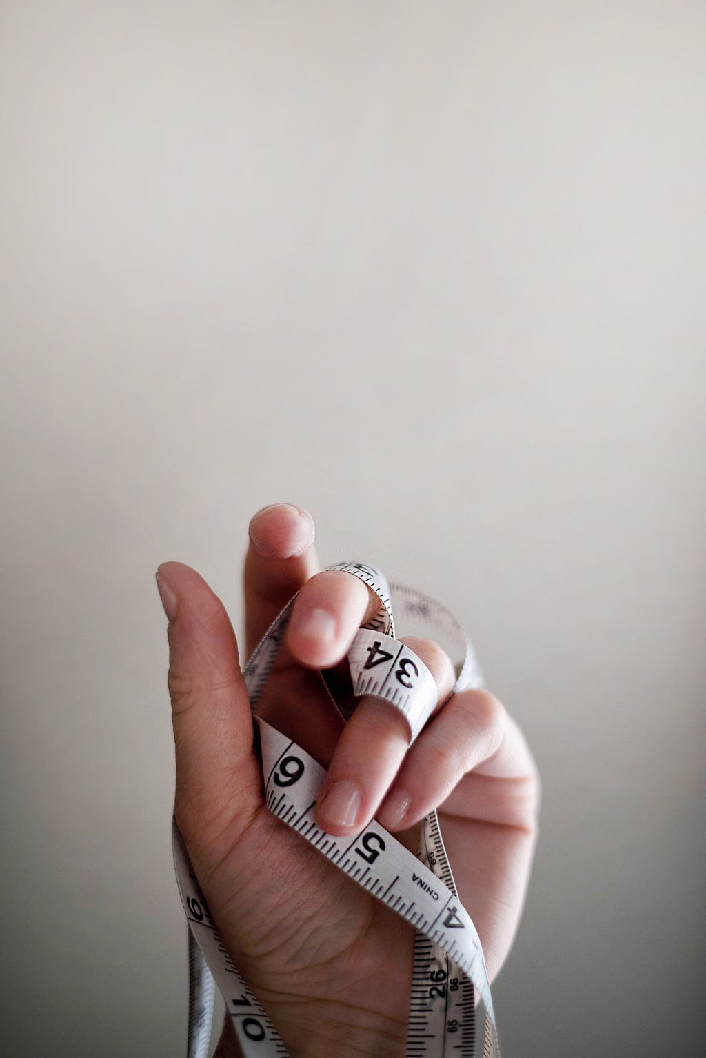 A person’s hand with a cloth measuring tape tangled up within it. The palm of the hand is facing the camera.