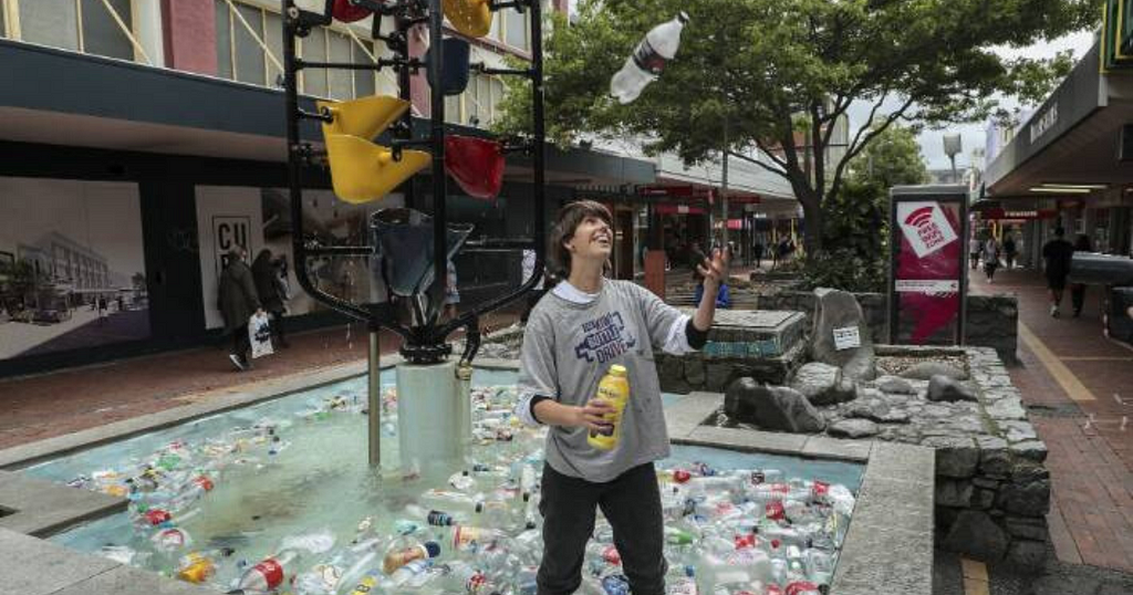 Holly standing in Wellington’s bucket fountain (filled with plastic) throwing a plastic bottle in the air