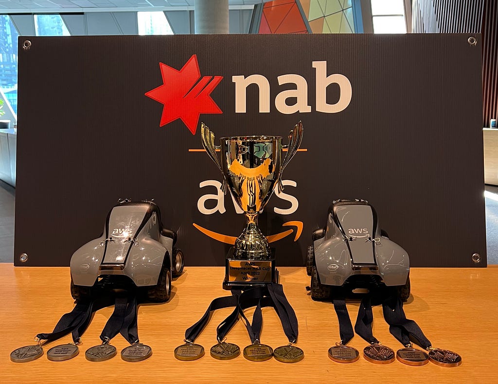 Two remote control cars, a trophy and medals placed in front of the NAB and AWS logos