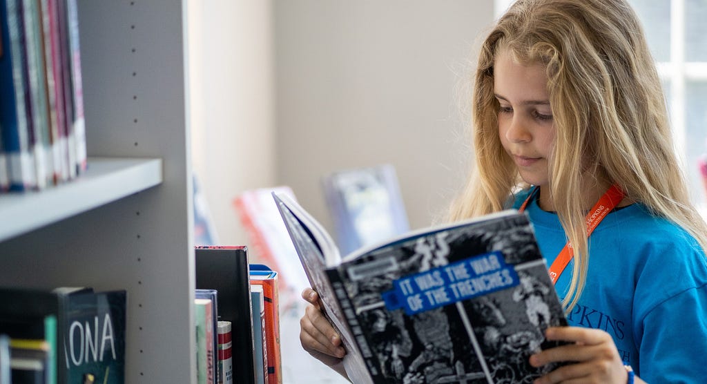 An image of a CTY student reading a book in front of a bookshelf.