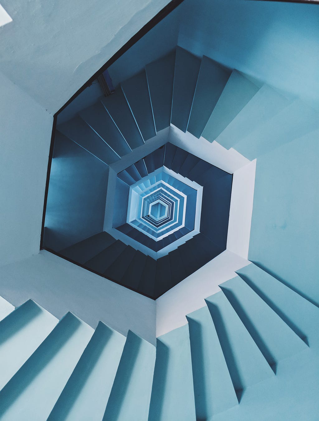 A photo of a view looking centrally down a blue hexagonal staircase that looks like it continues forever.