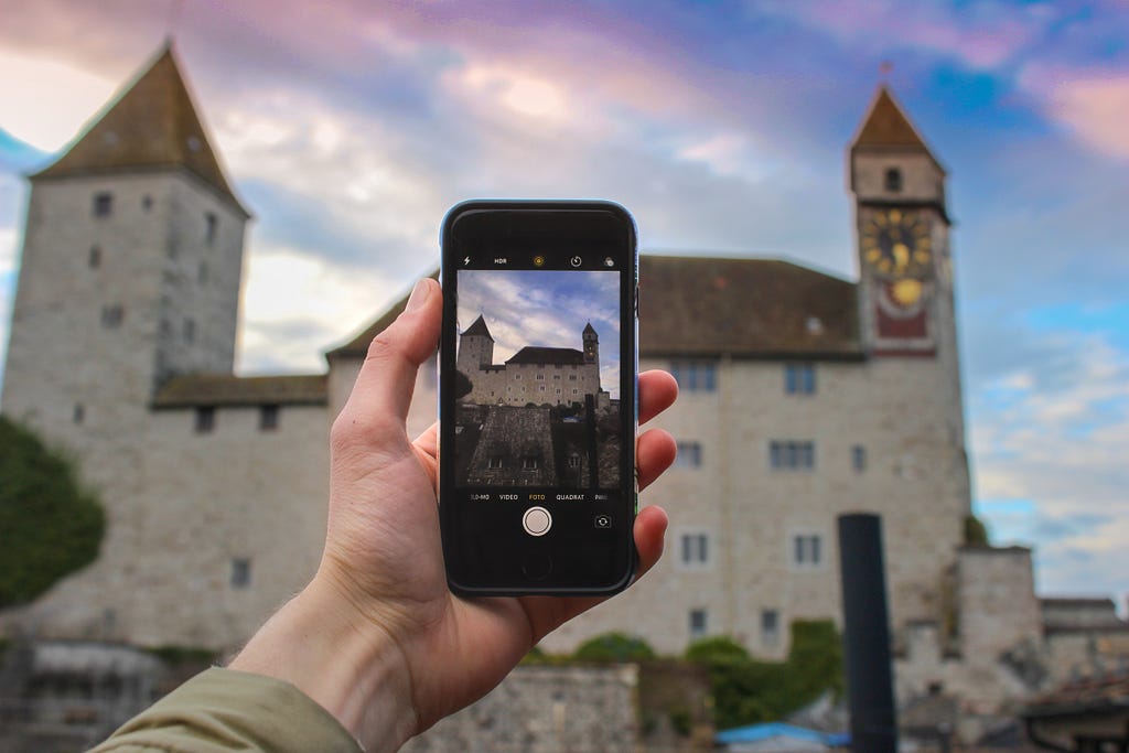 A mobile phone in camera mode being held up to take a photo of a castle.