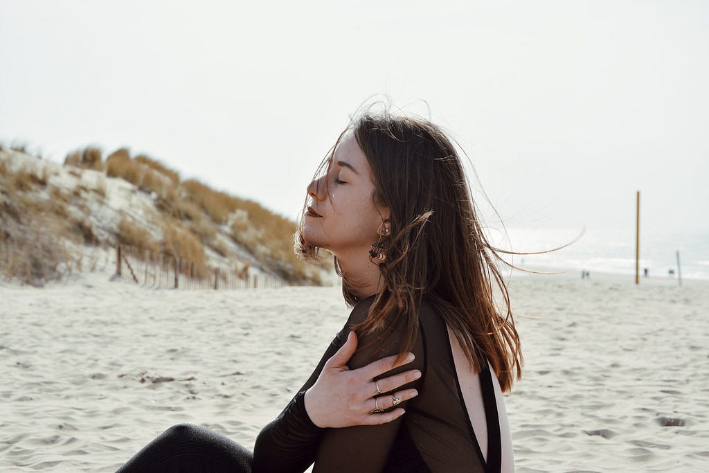 Money mindset: Woman on beach, hugging her chest, with eyes closed looking serene