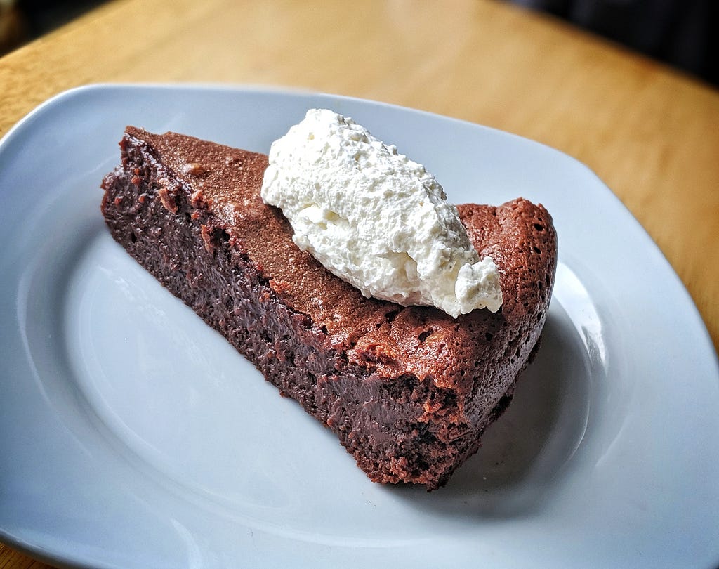 A slice of chocolate tart topped with a scoop of whipped cream