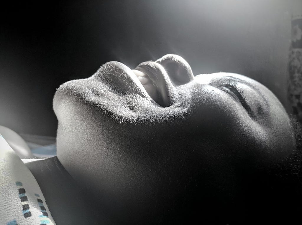 A  black-and-white side  of a lady smiling at sun rays.