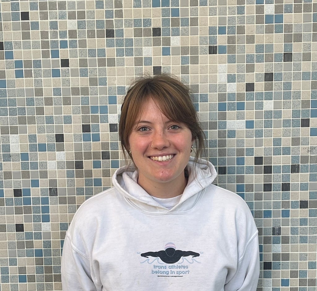 On September 25, 2022, in Pius Xii Memorial Library, Jackie Barnes stands in front of a multicolored tile background smiling hugely as she reflects that she does not have to take the biology test she helps her friend study for in the library.