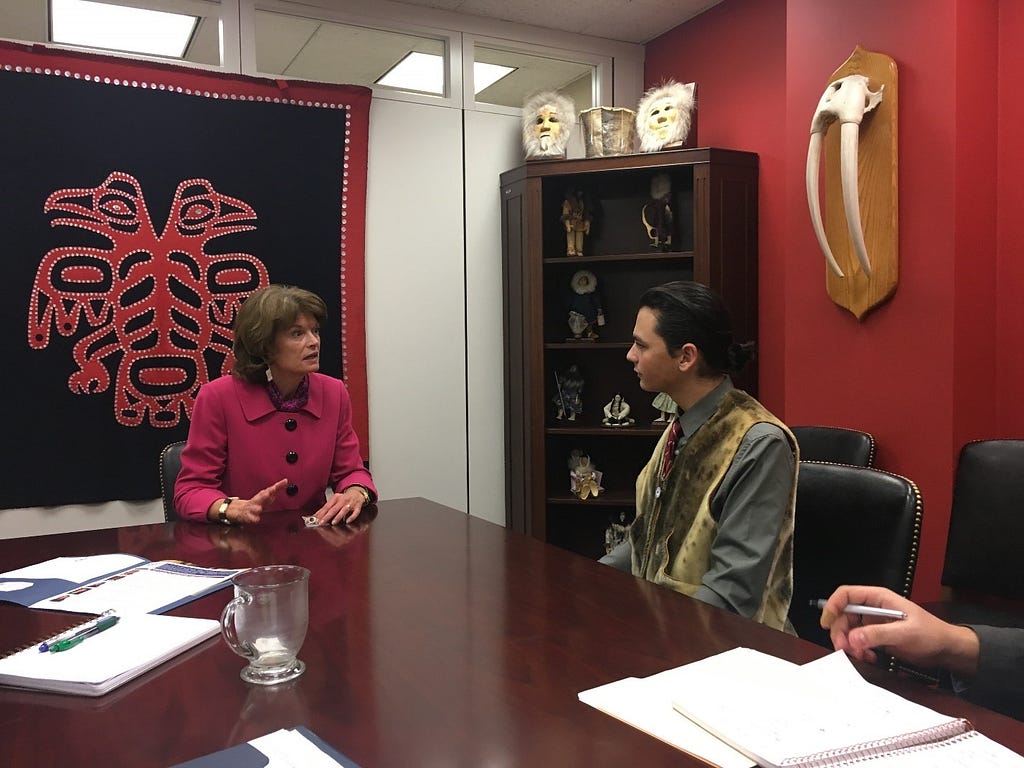 young man and woman senator in an office with Alaska Native Art decorating the walls