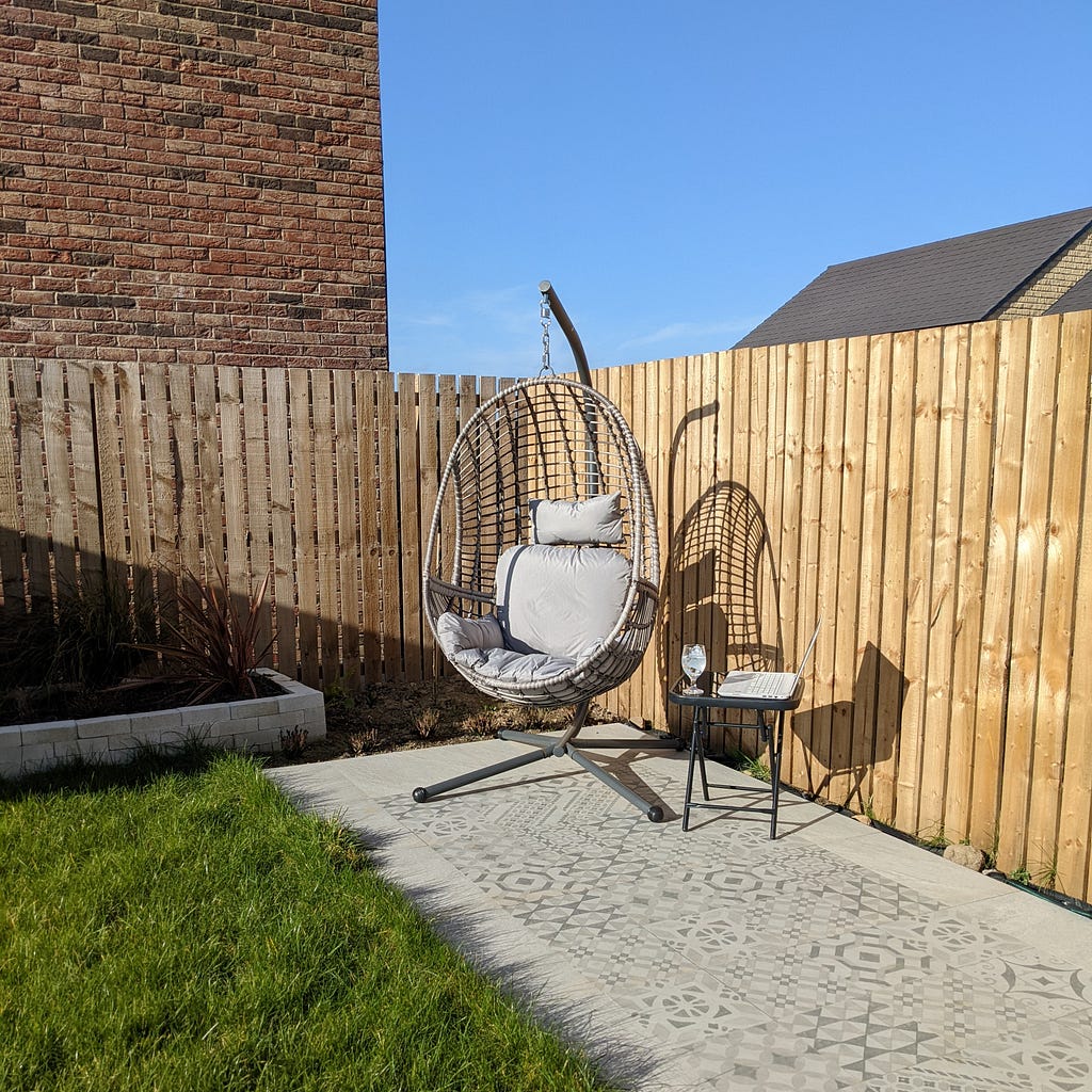 A grey hanging egg chair in a sunny garden.