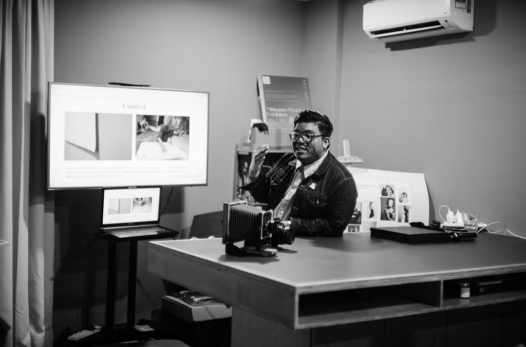 Emillio sitting at a desk across a screen with a presentation during his Analog photography workshop.