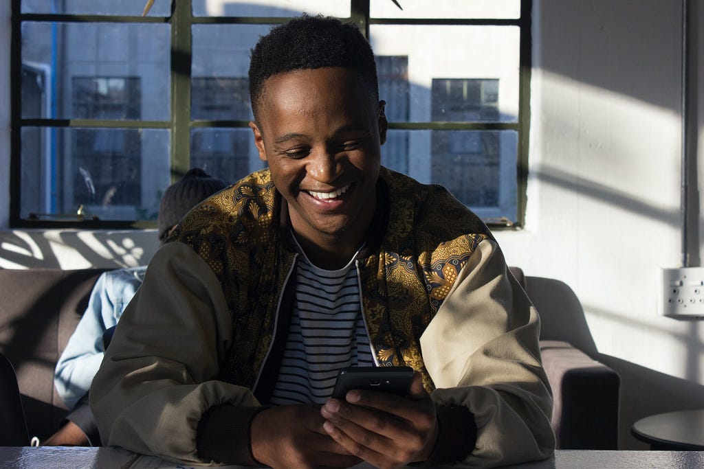 Homem negro sorrindo enquanto usa um smartphone
