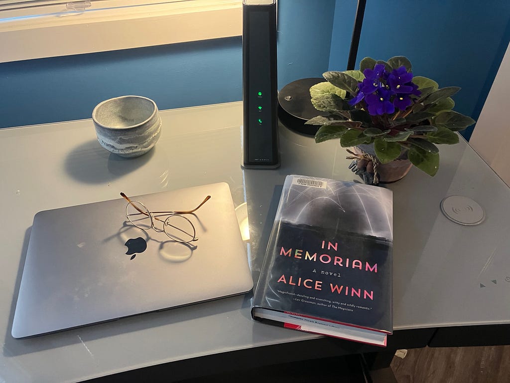In Memoriam, Alice Winn — book on desk next to laptop, eyeglasses, potted purple flowers