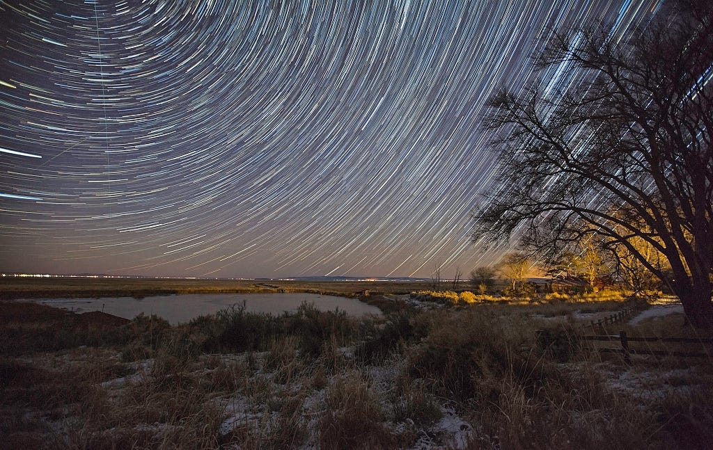 A long exposure shows starlight trailing in a circle over a desert landscape.