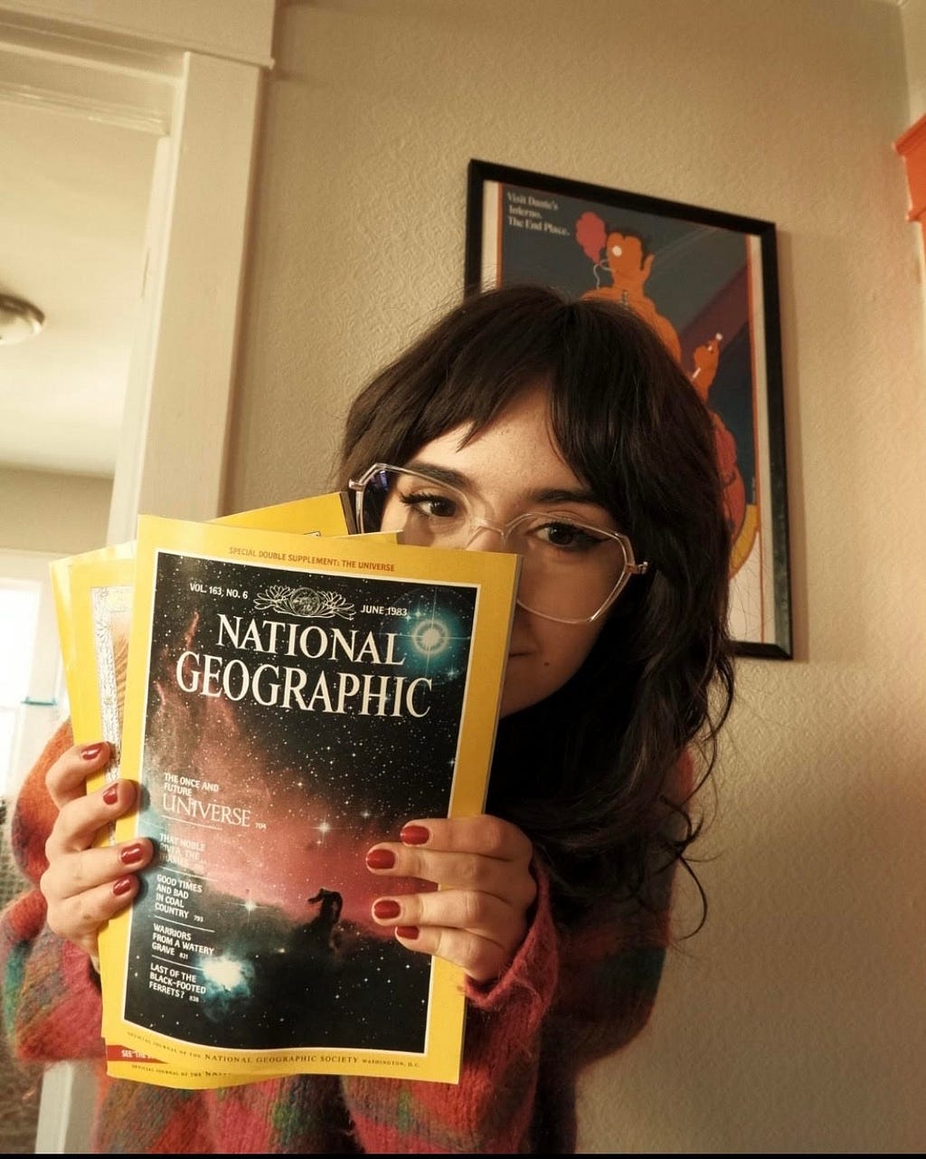 A close-up image of Tori O’Campo posing in front of a painting while holding National Geographic magazines, which are covering a part of her face.