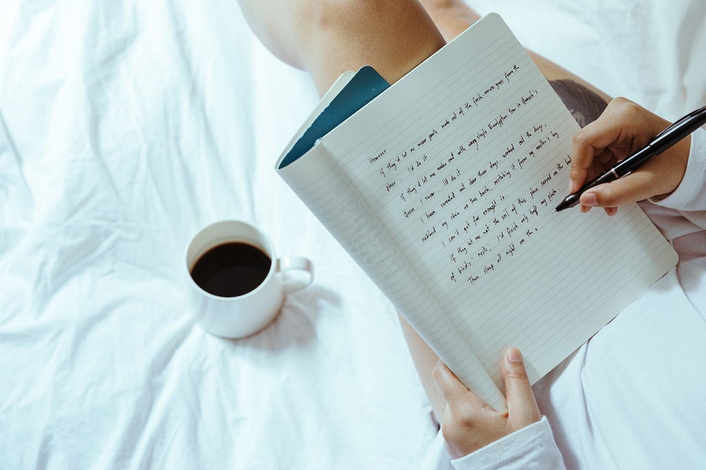 girl writing in bed on journal with coffee