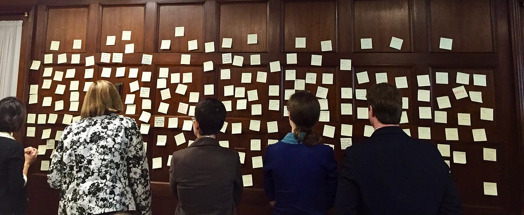 Photo of 5 people standing in front of a wall filled with yellow sticky notes.