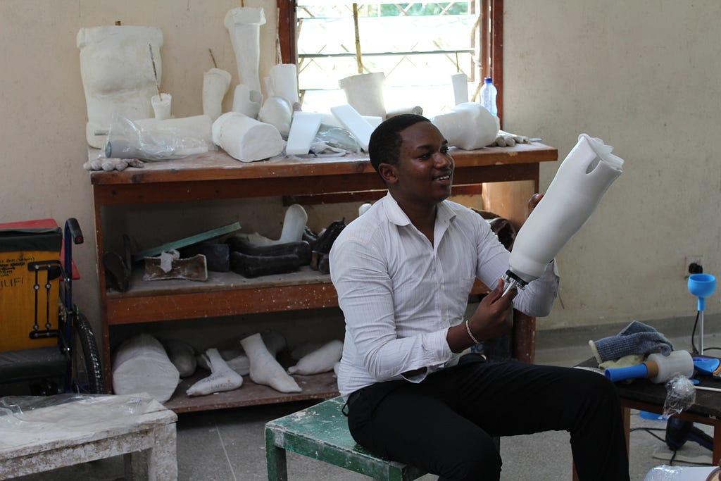 A man is sitting in a prosthetics clinic, holding a prosthetic leg.