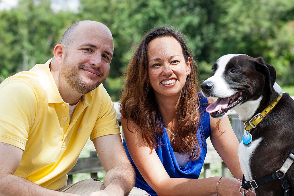 A man in a yellow shirt, a lady in a blue shirt and a black and white dog