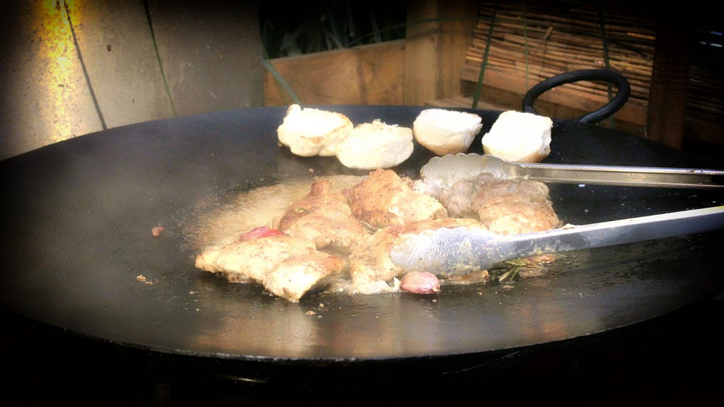 Chicken pieces frying on the tawa with breads warming on the edge