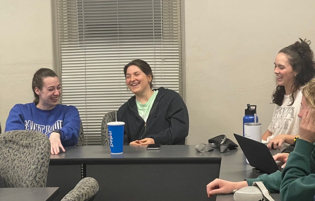 Four students sitting in a classroom and laughing.