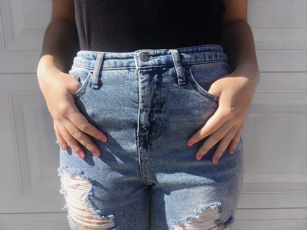 Light blue high-waisted jeans with a few holes in them. Hands in pockets in the front.