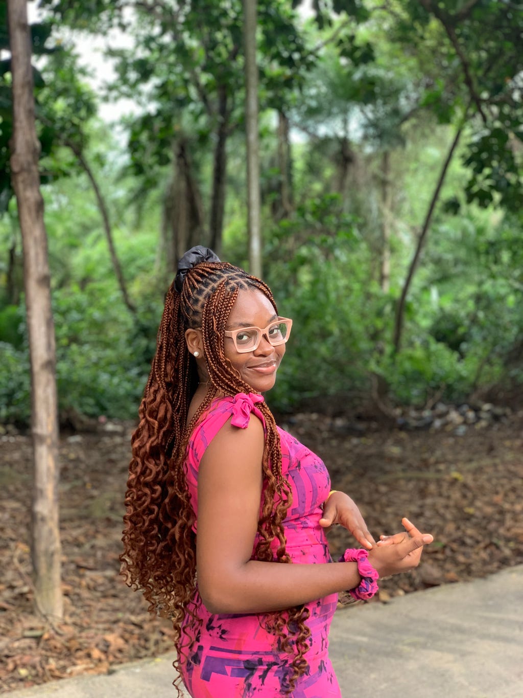 Doreen smiling in a pink dress, wearing a nude coloured pair of glasses and knotless braids.