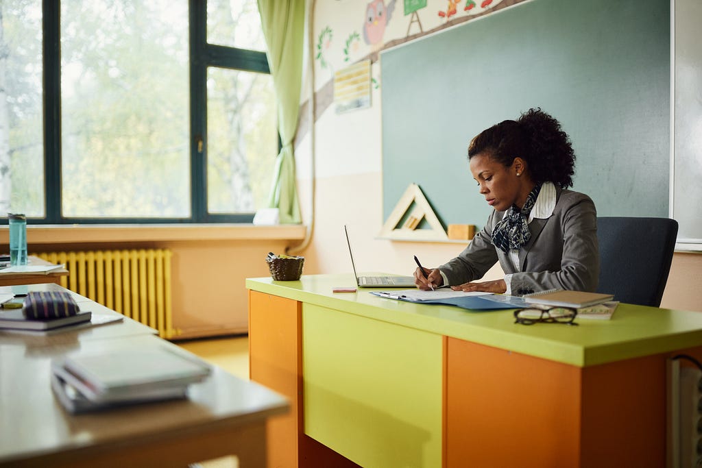 Teacher at desk in classroom. Photo by skynesher/Getty Images