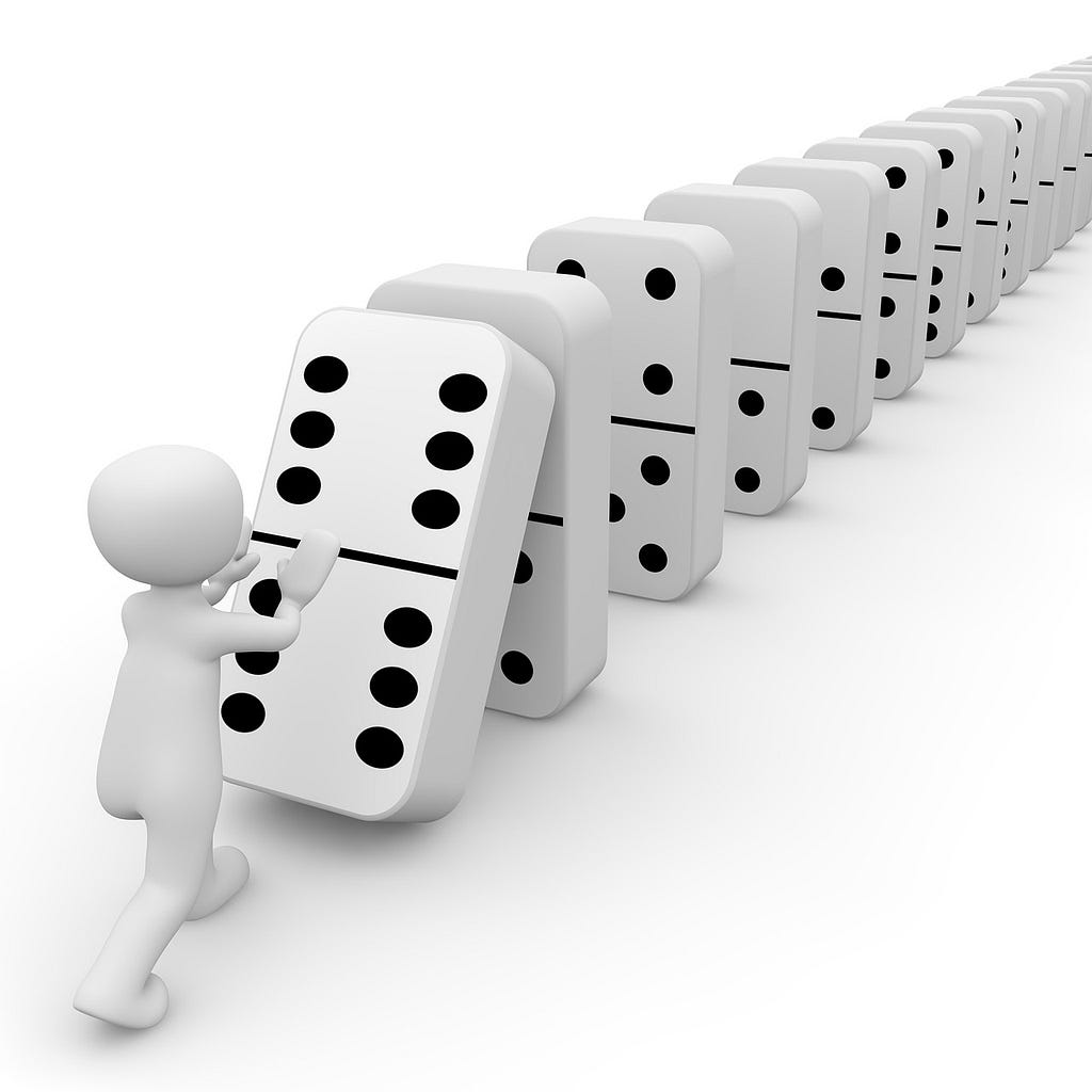 A person pushing one domino with their hands, at the end of an array of upright dominoes