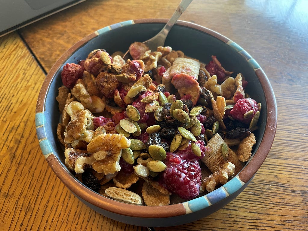 A bowl of whole-grain cereal topped with berries, walnuts, raisins, pumpkin seeds, and cinnamon.