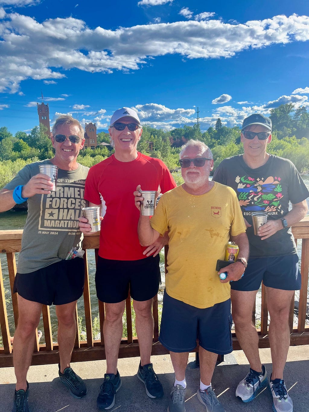 Four middle-aged men in sunglasses and running clothes holding beer cups