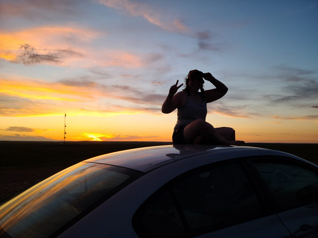 Anne sitting on the roof of her car at sunset