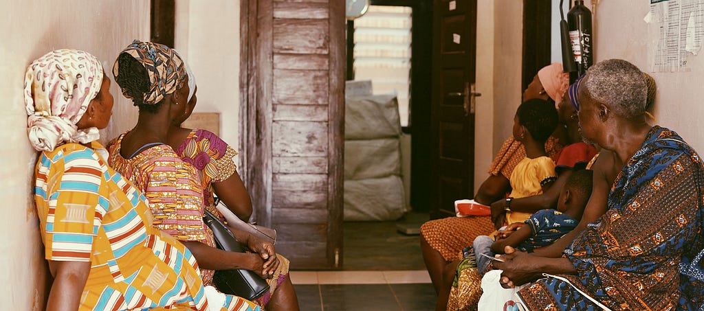 Patients in the waiting hall of Atwereboana CHPS compound, Ghana, sit in front of an open door