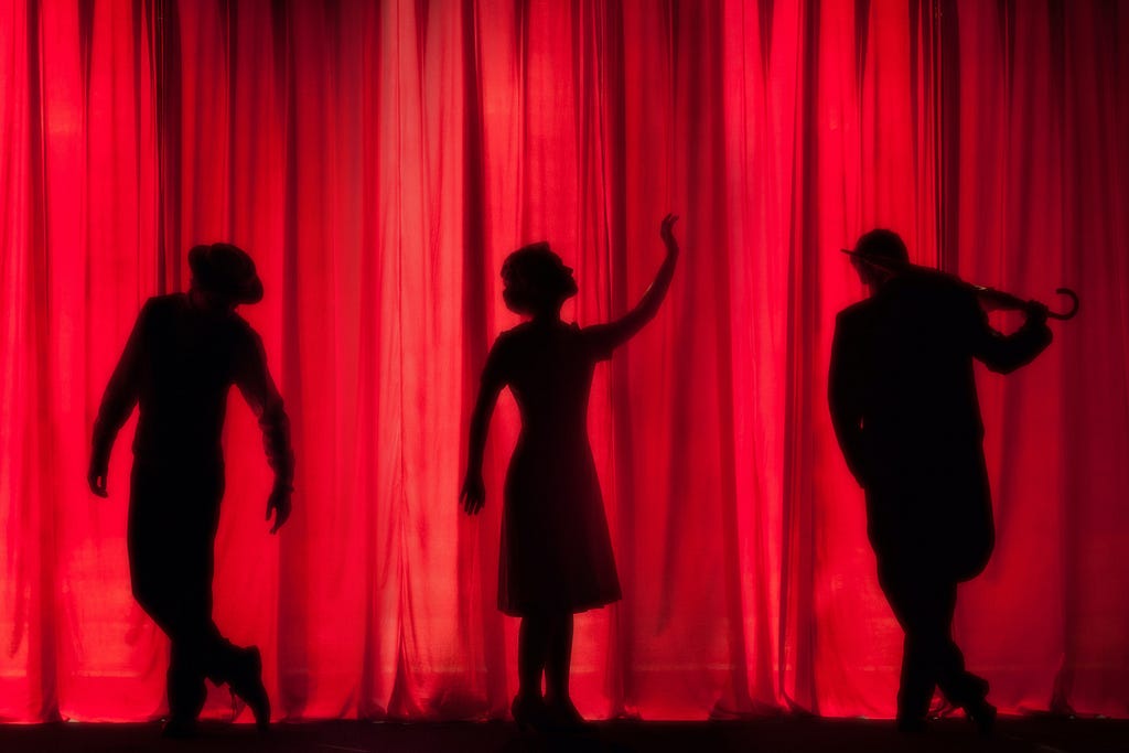 Three performers silhouetted against a red theatre curtain