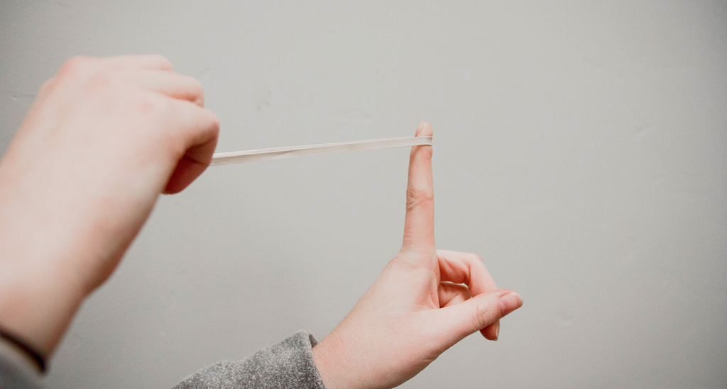 Only a person’s hands are visible, they are pulling a rubber band which is about to snap