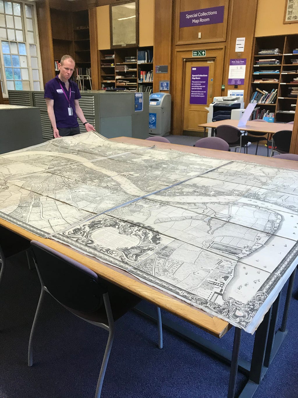 A view of the University of Manchester Library Map Room, with a large map of London being opened up by a member of our Readers Services Team