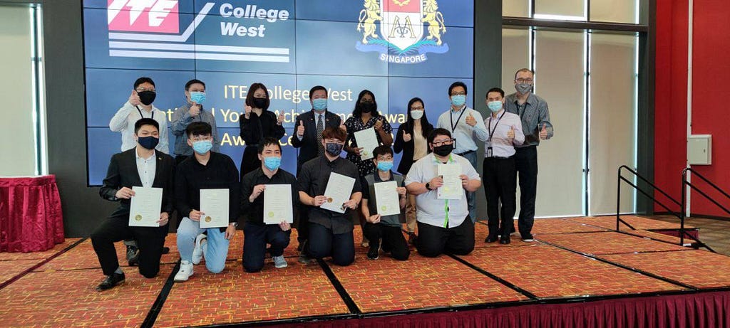 Students kneeling on stage with their NYAA certificates, posing for a photo.